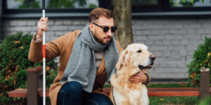 Blind person petting a service dog while stopping in the park.