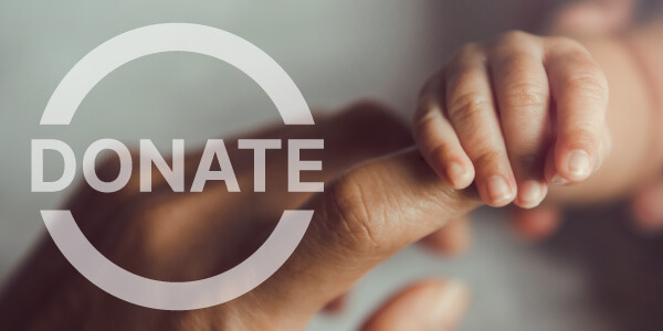A small baby holds an adult finger with a Donate logo