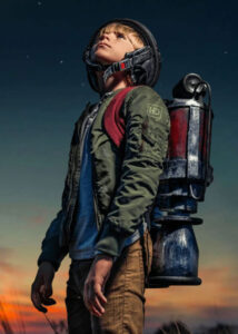 A boy in a jet pack prepares for launch in front of a colorful sky.