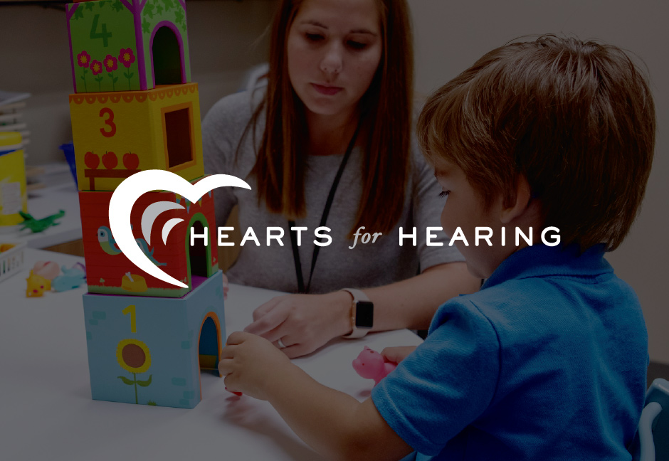 Hearts for hearing logo in front of darkened background of patient and therapist working together