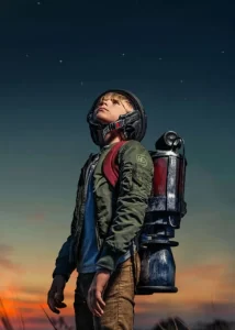 A boy in a jet pack prepares for launch in front of a colorful sky.