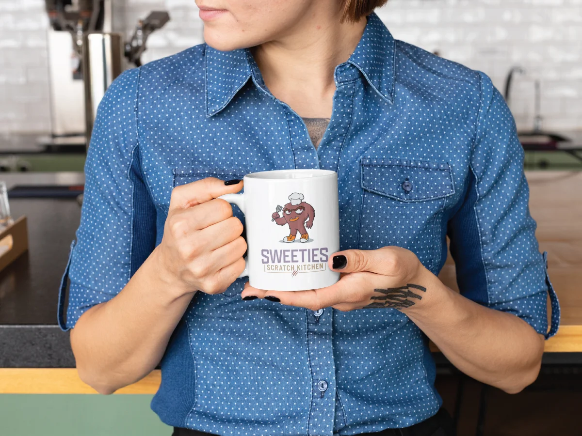 sweeties scratch kitchen logo mockup on coffee mug being held by adult female in denim shirt